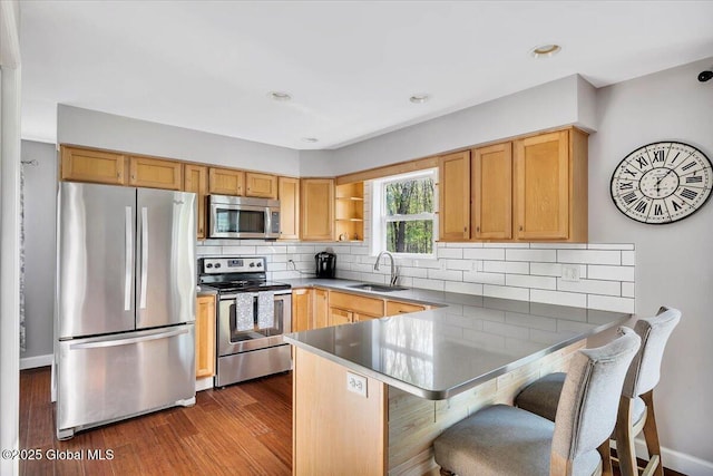 kitchen with appliances with stainless steel finishes, a sink, a peninsula, decorative backsplash, and a breakfast bar