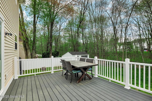 wooden terrace featuring outdoor dining space and an outbuilding