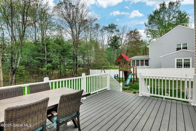 deck with a playground, outdoor dining area, and view of wooded area