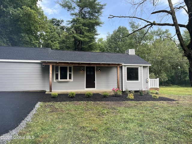 ranch-style house with a chimney, a shingled roof, a porch, aphalt driveway, and a front lawn