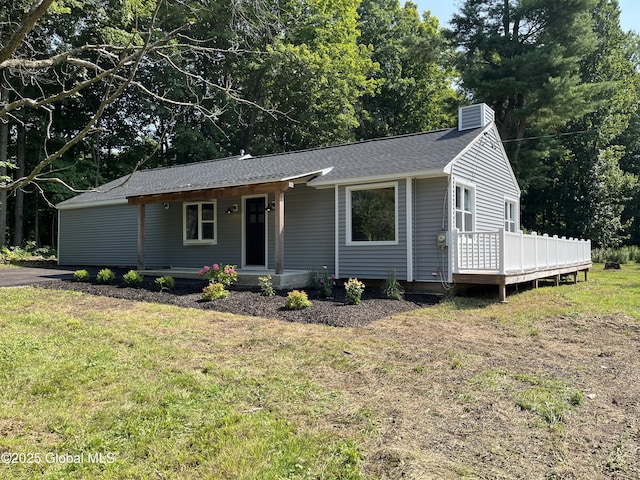 ranch-style house with a chimney, a porch, a wooden deck, roof with shingles, and a front lawn