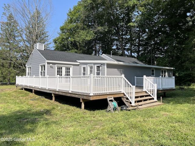 rear view of property featuring a chimney, a deck, a shingled roof, and a yard
