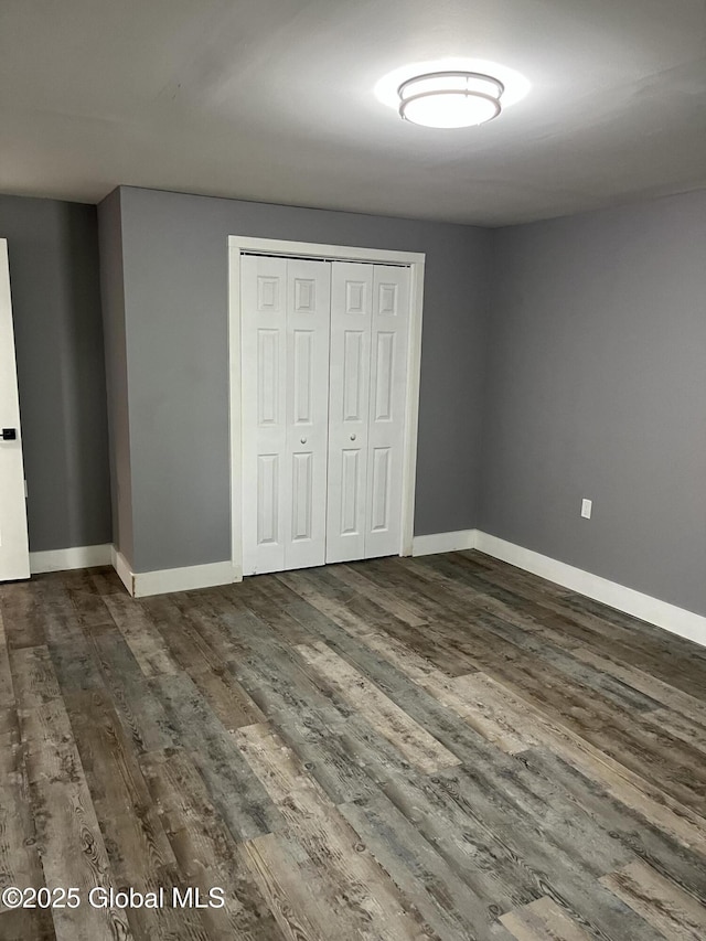 unfurnished bedroom with baseboards, a closet, and dark wood-type flooring