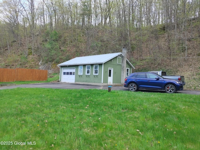 view of outdoor structure with driveway, an outbuilding, a wooded view, and fence