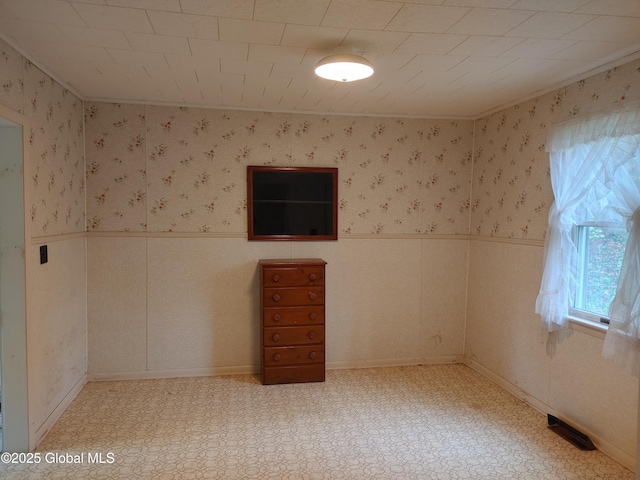 spare room featuring light floors, visible vents, wallpapered walls, and a wainscoted wall