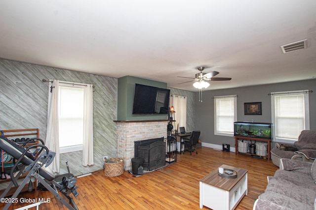 living room featuring a ceiling fan, light wood-style flooring, visible vents, and an accent wall