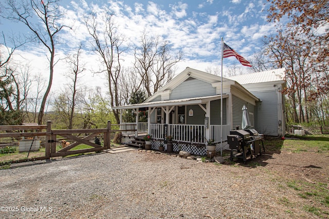 farmhouse inspired home featuring a porch, a gate, fence, and metal roof