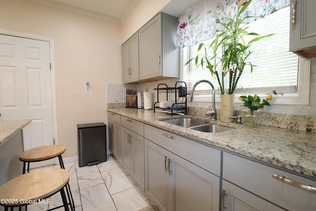 kitchen featuring gray cabinets, a sink, light marble finish flooring, decorative backsplash, and light stone counters