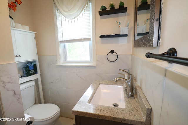 half bathroom featuring toilet, vanity, tile walls, and wainscoting