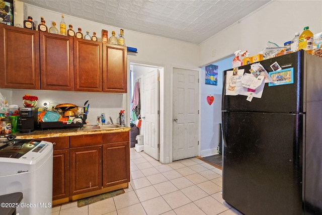 kitchen with a sink, freestanding refrigerator, light countertops, light tile patterned flooring, and washer / clothes dryer