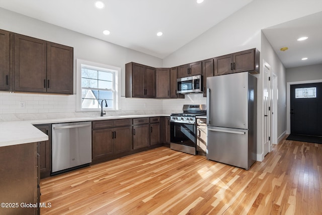 kitchen with a sink, dark brown cabinetry, decorative backsplash, light wood-style floors, and stainless steel appliances