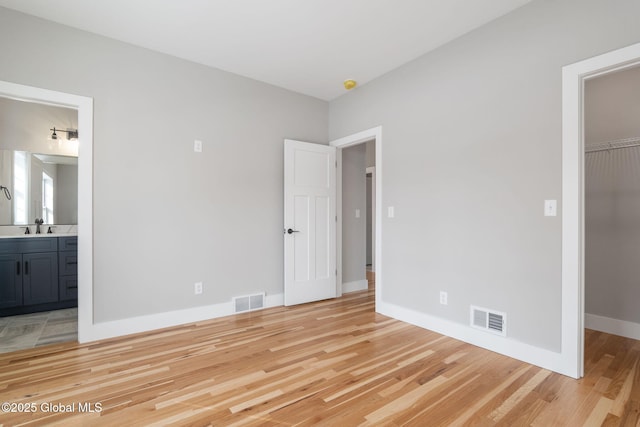 unfurnished bedroom featuring a spacious closet, light wood finished floors, visible vents, and a closet