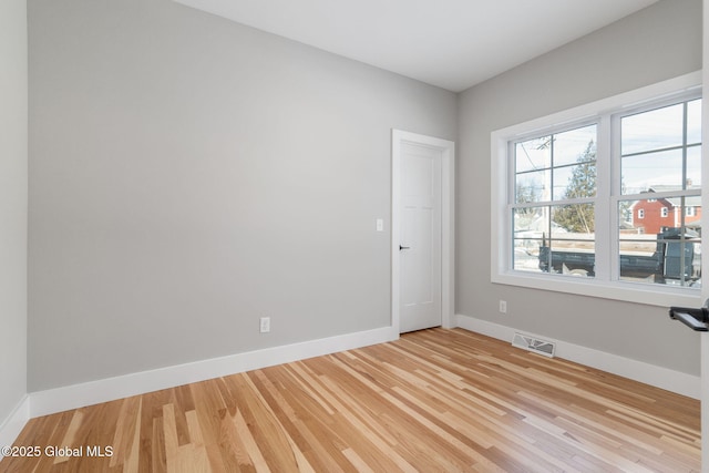 empty room with baseboards, light wood finished floors, and visible vents