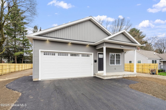 view of front of house featuring an attached garage, board and batten siding, fence, and aphalt driveway