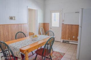 dining room featuring light tile patterned floors, a baseboard radiator, wooden walls, and a wainscoted wall