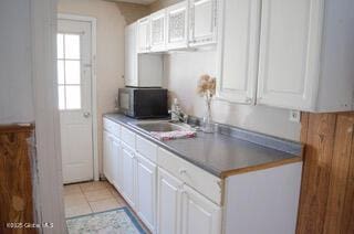 kitchen featuring white cabinets, light tile patterned floors, a sink, and black microwave