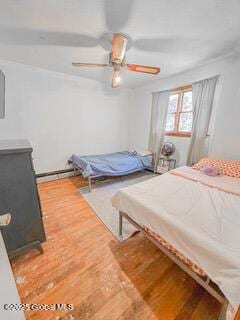 bedroom with a baseboard heating unit, a ceiling fan, and wood finished floors