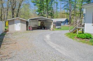 view of vehicle parking featuring a detached carport, a storage shed, stairway, and driveway