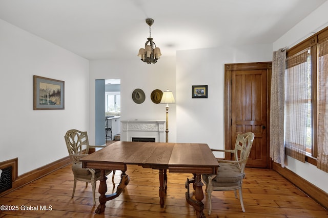 dining room with a chandelier, a fireplace, light wood-style flooring, and baseboards