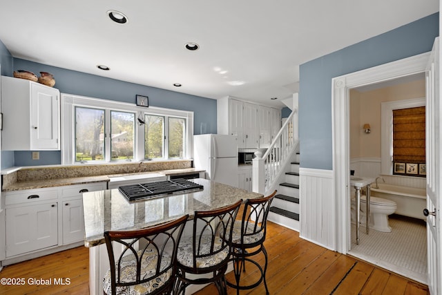 kitchen featuring appliances with stainless steel finishes, white cabinets, a center island, light wood-style floors, and a wainscoted wall