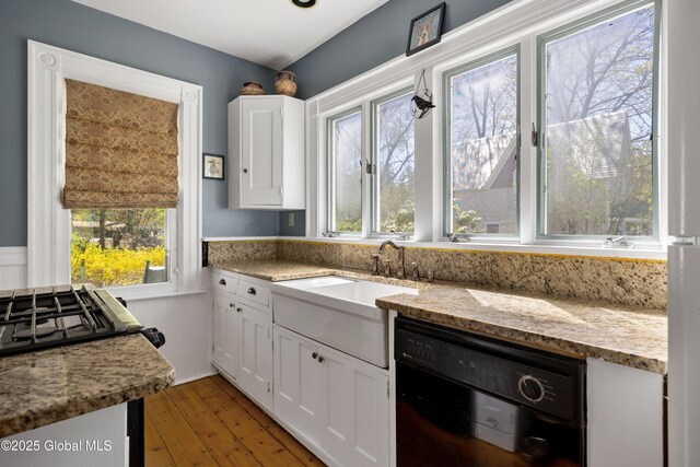 kitchen with black dishwasher, white cabinetry, light wood finished floors, light stone counters, and a sink