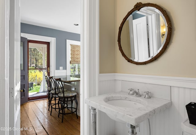 bathroom featuring a wainscoted wall, hardwood / wood-style flooring, a sink, and a decorative wall