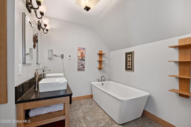 bathroom featuring baseboards, lofted ceiling, a freestanding tub, and double vanity