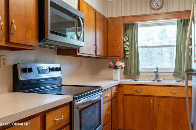 188 Fort Edward Rd, Moreau, NY 12828 - kitchen with stainless steel appliances, a sink, brown cabinets, plenty of natural light, and wallpapered walls
