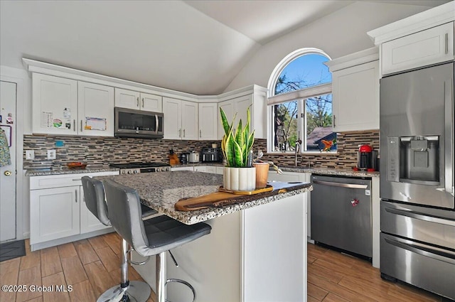 kitchen featuring stainless steel appliances, lofted ceiling, light wood-type flooring, white cabinetry, and decorative backsplash