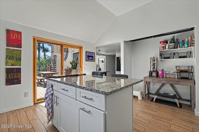 kitchen featuring light wood-style flooring, lofted ceiling, white cabinetry, light stone counters, and a kitchen island