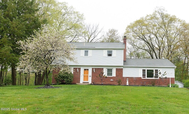 colonial house featuring a chimney, brick siding, and a front lawn