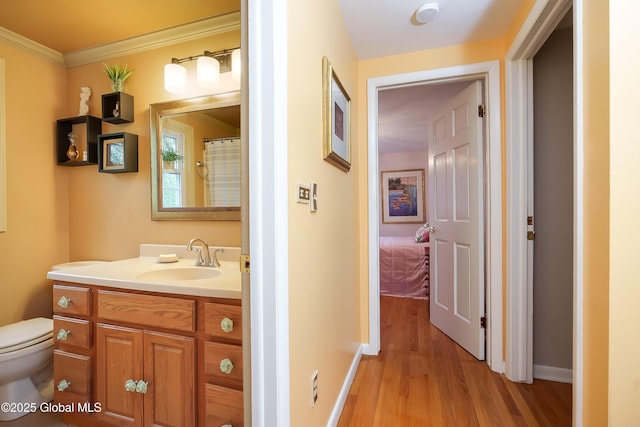 bathroom featuring toilet, wood finished floors, vanity, ornamental molding, and baseboards
