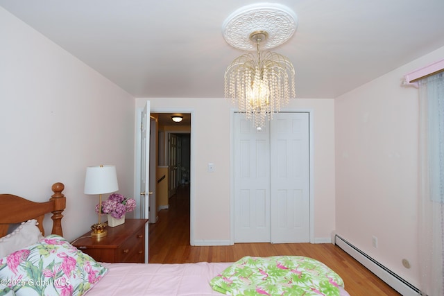 bedroom featuring a baseboard radiator, a chandelier, wood finished floors, and a closet