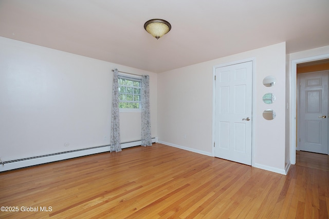unfurnished room with a baseboard heating unit, light wood finished floors, and baseboards