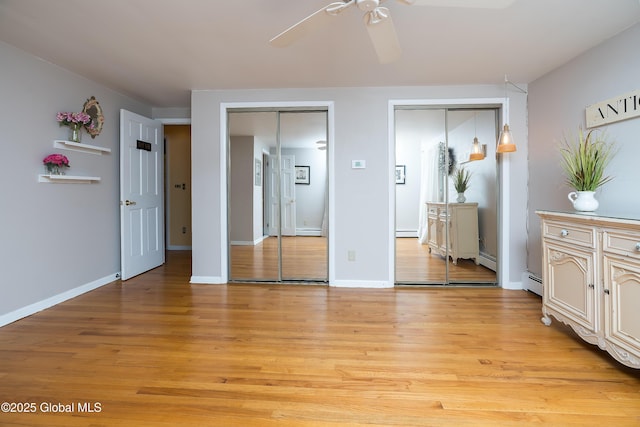 bedroom featuring two closets, baseboard heating, light wood finished floors, and baseboards