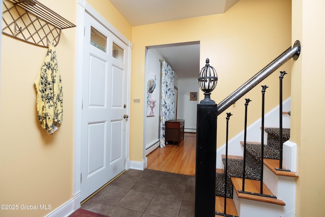 entryway with dark tile patterned flooring, baseboard heating, stairs, and baseboards