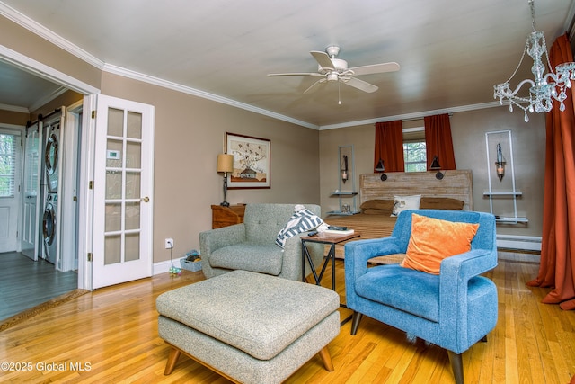 living area with stacked washing machine and dryer, healthy amount of natural light, a baseboard heating unit, a ceiling fan, and ornamental molding