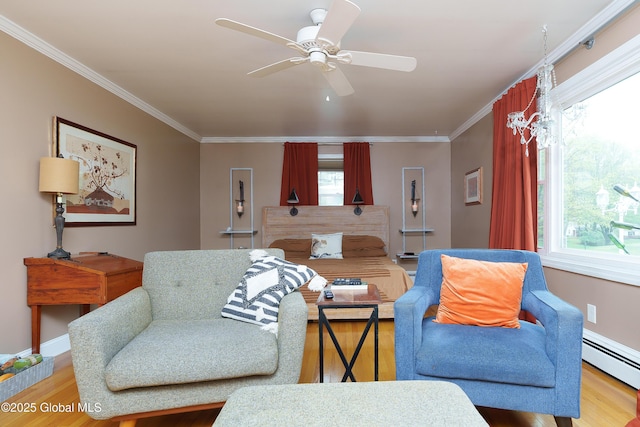 living area with baseboard heating, wood finished floors, ornamental molding, a ceiling fan, and baseboards