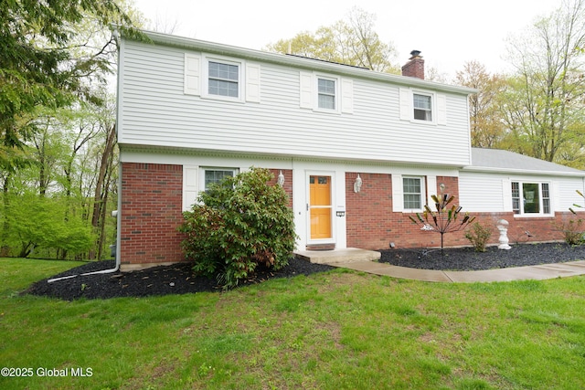 colonial-style house featuring brick siding, a chimney, and a front yard