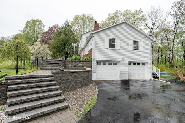 view of property exterior featuring stairway, asphalt driveway, a garage, and a chimney