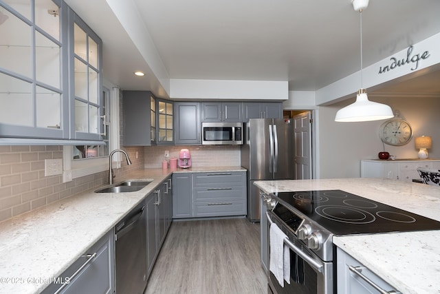kitchen featuring appliances with stainless steel finishes, a sink, gray cabinetry, light stone countertops, and backsplash