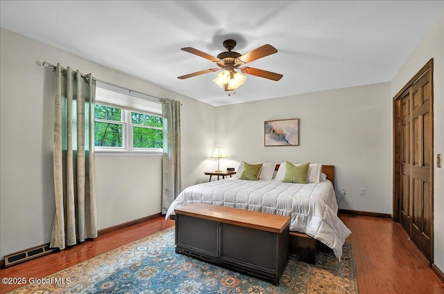 bedroom with a ceiling fan, visible vents, wood finished floors, and baseboards