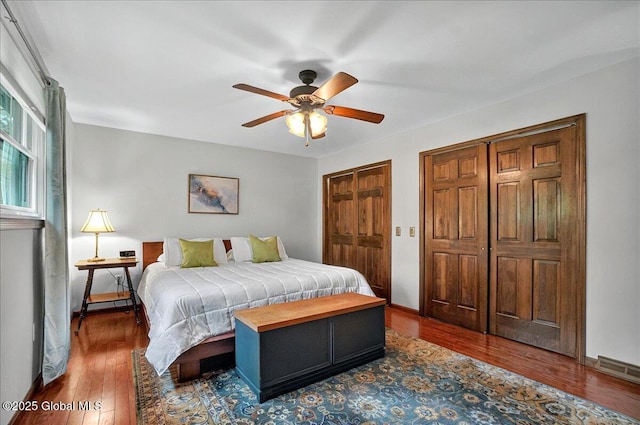 bedroom with a ceiling fan, wood-type flooring, multiple closets, visible vents, and baseboards