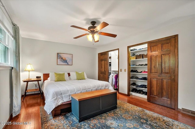 bedroom featuring a ceiling fan, a closet, baseboards, a walk in closet, and wood finished floors