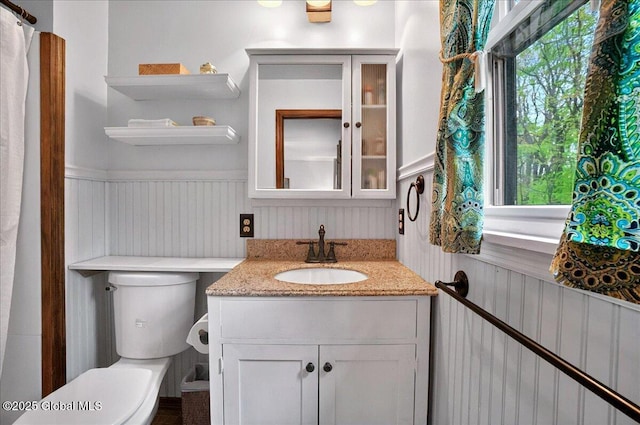 bathroom with wainscoting, vanity, toilet, and a healthy amount of sunlight