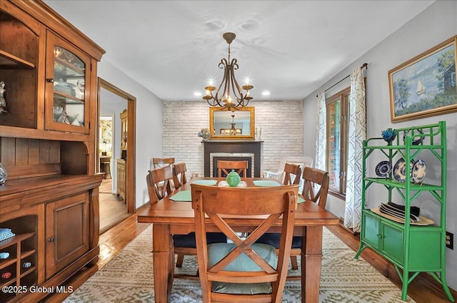 dining area with light wood finished floors, a chandelier, a brick fireplace, and recessed lighting