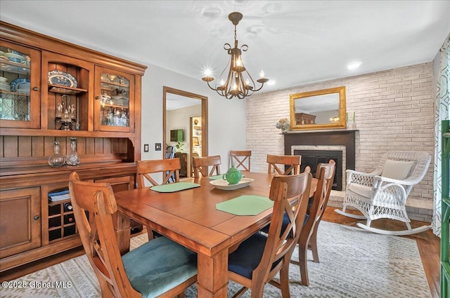 dining area featuring a chandelier, wood finished floors, a fireplace, and brick wall