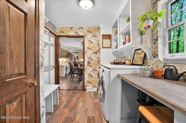 clothes washing area featuring light wood finished floors, wallpapered walls, washer and dryer, and a healthy amount of sunlight