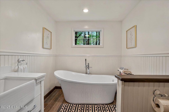 bathroom with wainscoting, a freestanding bath, and wood finished floors