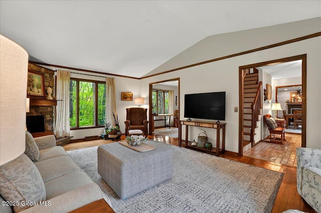 living area with vaulted ceiling, baseboards, a stone fireplace, and wood finished floors